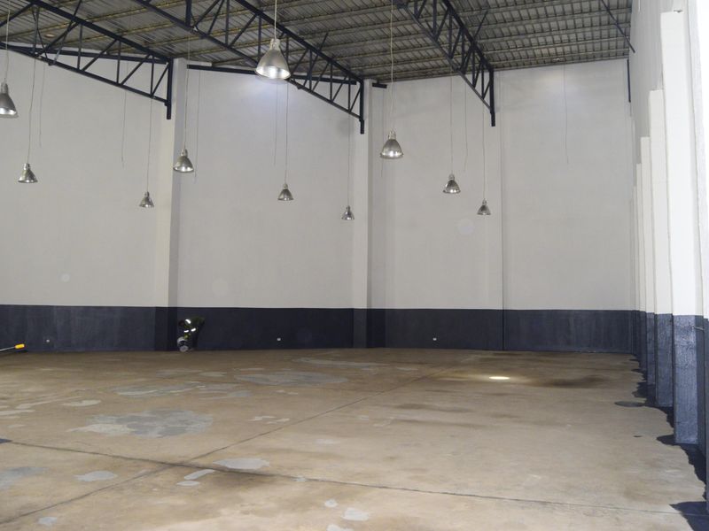 Spacious industrial warehouse unit featuring high ceilings with exposed steel trusses, pendant lighting, and durable concrete flooring.