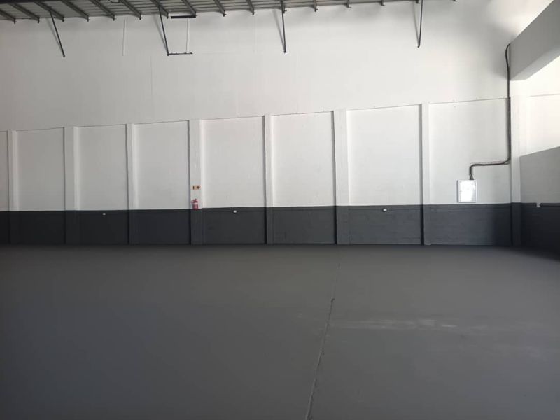 Spacious industrial utility area featuring high ceilings with exposed steel trusses, durable painted concrete flooring, and clean, freshly painted walls.