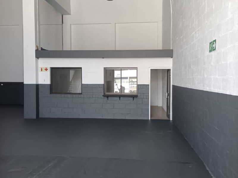 Spacious industrial utility area featuring high ceilings with exposed steel trusses, painted concrete block walls, and a mezzanine level with an integrated office partition.