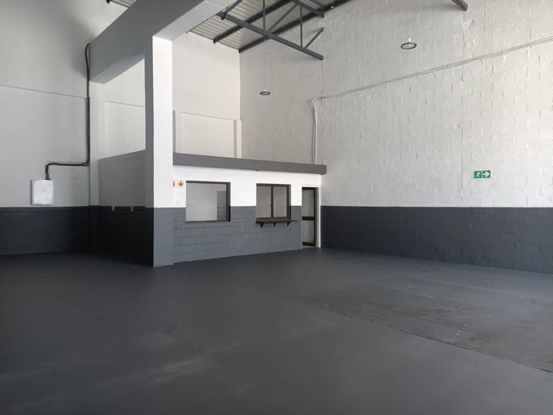 Spacious industrial warehouse unit featuring high ceilings with exposed steel trusses, durable epoxy flooring, and a dedicated internal office or service area.