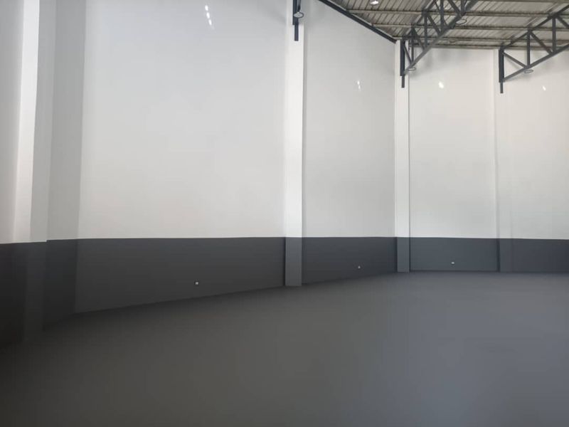 Spacious industrial warehouse interior featuring high ceilings with exposed steel trusses, durable epoxy flooring, and clean, freshly painted walls.
