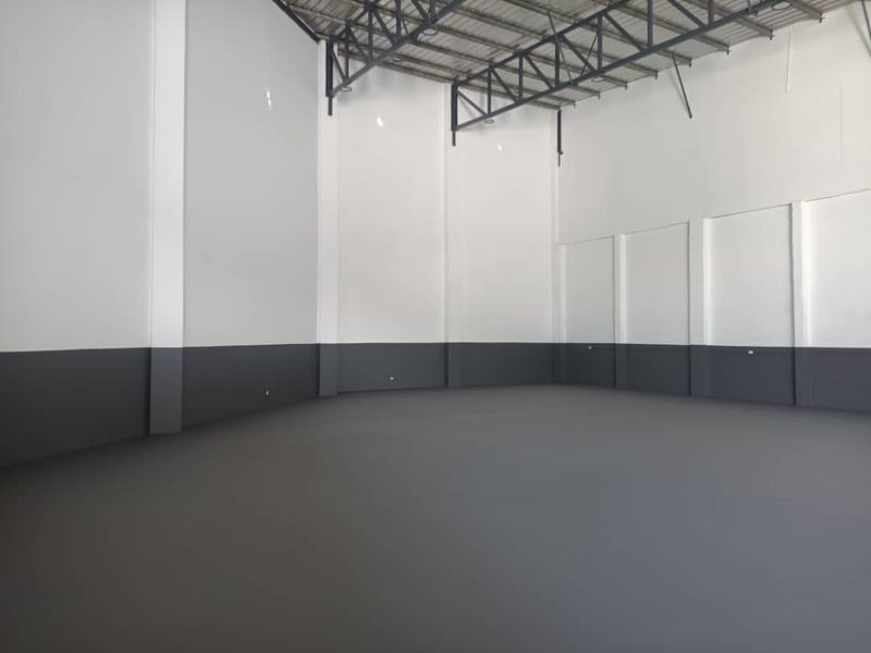 Spacious industrial warehouse unit featuring high ceilings with exposed steel trusses, durable epoxy flooring, and freshly painted walls, ideal for storage or light manufacturing.
