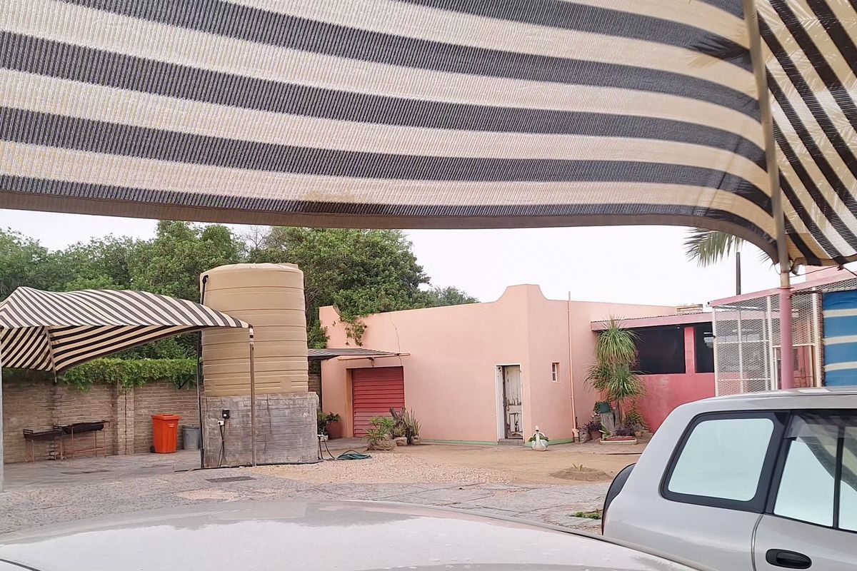 Exterior view of the property grounds featuring a large water storage tank, shaded parking area, and perimeter walling.