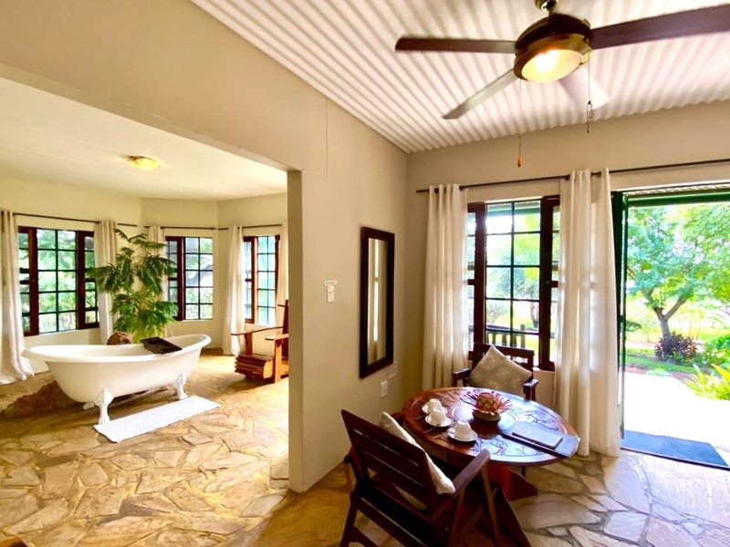 Spacious lodge bedroom featuring unique stone flooring, a freestanding bathtub, and direct access to the garden through large multi-pane windows.