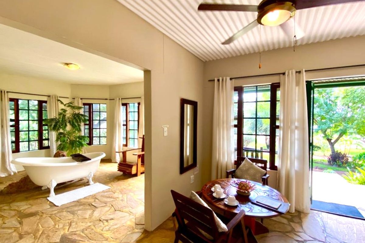 Spacious lodge bedroom featuring unique stone flooring, a freestanding bathtub, and direct access to the garden through large multi-pane windows.