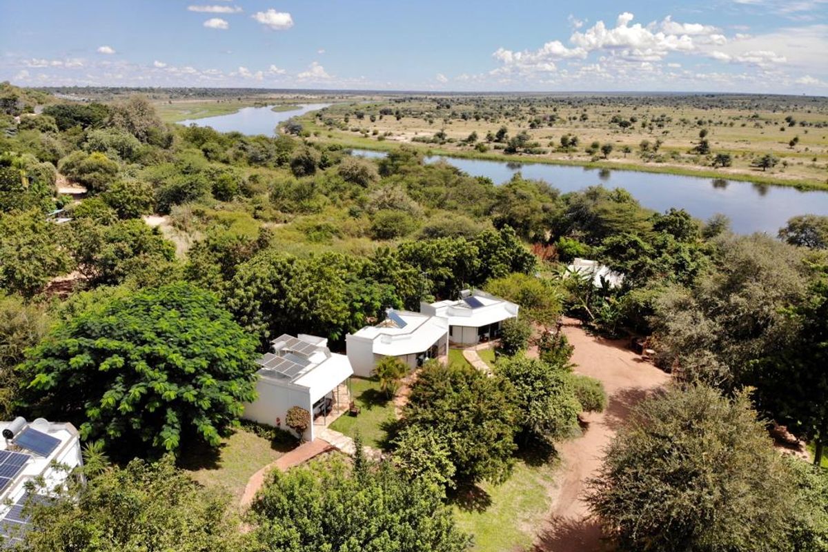 Aerial view of the lodge property featuring multiple units with solar panels, set within a lush garden landscape overlooking a scenic river.