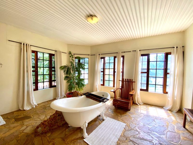 A spacious bathroom featuring a classic clawfoot bathtub, natural stone flooring, and large grid-pattern windows that provide ample natural light.