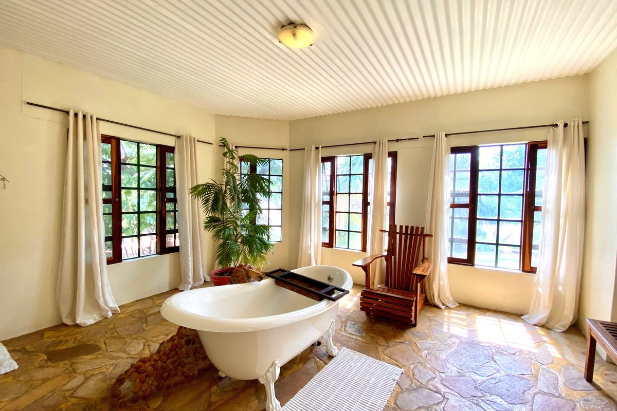 A spacious bathroom featuring a classic clawfoot bathtub, natural stone flooring, and large grid-pattern windows that provide ample natural light.