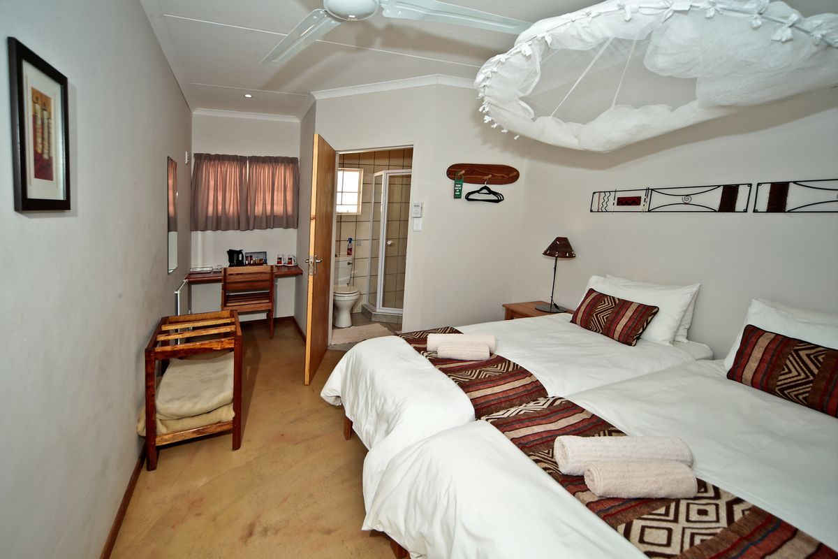 A hotel bedroom featuring twin beds, a ceiling fan, and an attached bathroom with a shower enclosure.
