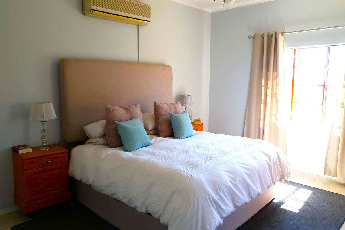 A well-lit bedroom featuring a wall-mounted air conditioning unit, tiled flooring, and direct access to an outdoor area through a glass door.
