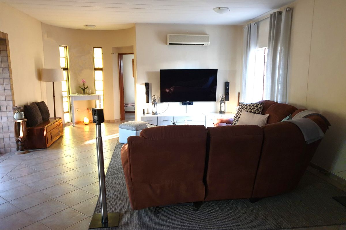 A comfortable living room featuring tiled flooring, a wall-mounted air conditioning unit, and large windows that allow for natural light.