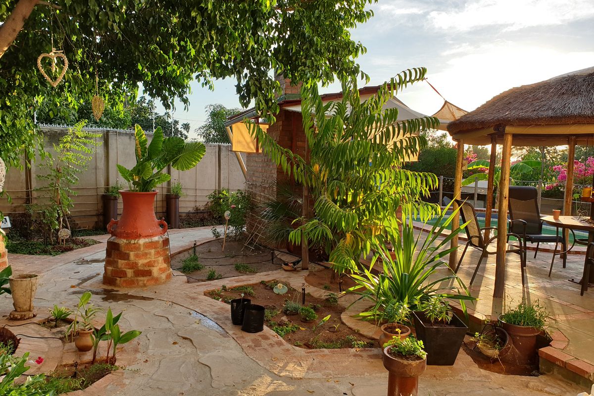A landscaped rear garden featuring a paved walkway, brick-built outdoor fireplace, and a thatched gazebo area, creating a relaxed outdoor living space.