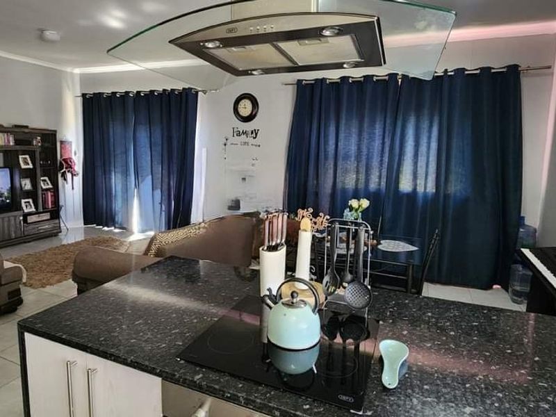 Open-plan living area featuring a kitchen island with granite countertops, integrated electric hob, and extractor fan, flowing into the dining and lounge space.