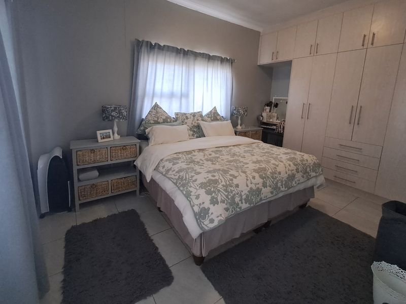 A well-maintained bedroom featuring neutral tiled flooring, ample built-in cupboard storage, and classic cornice detailing.