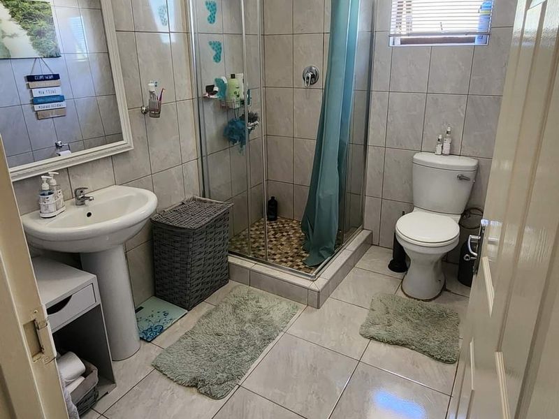A functional bathroom featuring a pedestal basin, a glass-enclosed shower, and a toilet, finished with neutral floor and wall tiling.