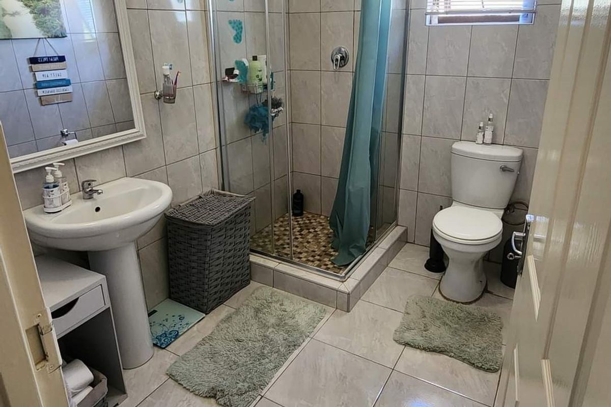 A functional bathroom featuring a pedestal basin, a glass-enclosed shower, and a toilet, finished with neutral floor and wall tiling.