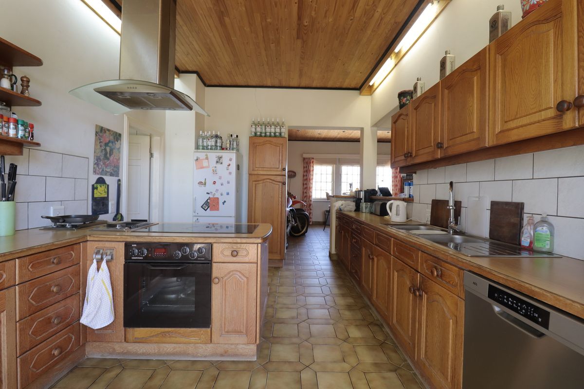 A functional kitchen featuring wooden cabinetry, tiled flooring, a built-in oven, hob, extractor fan, and a double sink with tiled splashbacks.