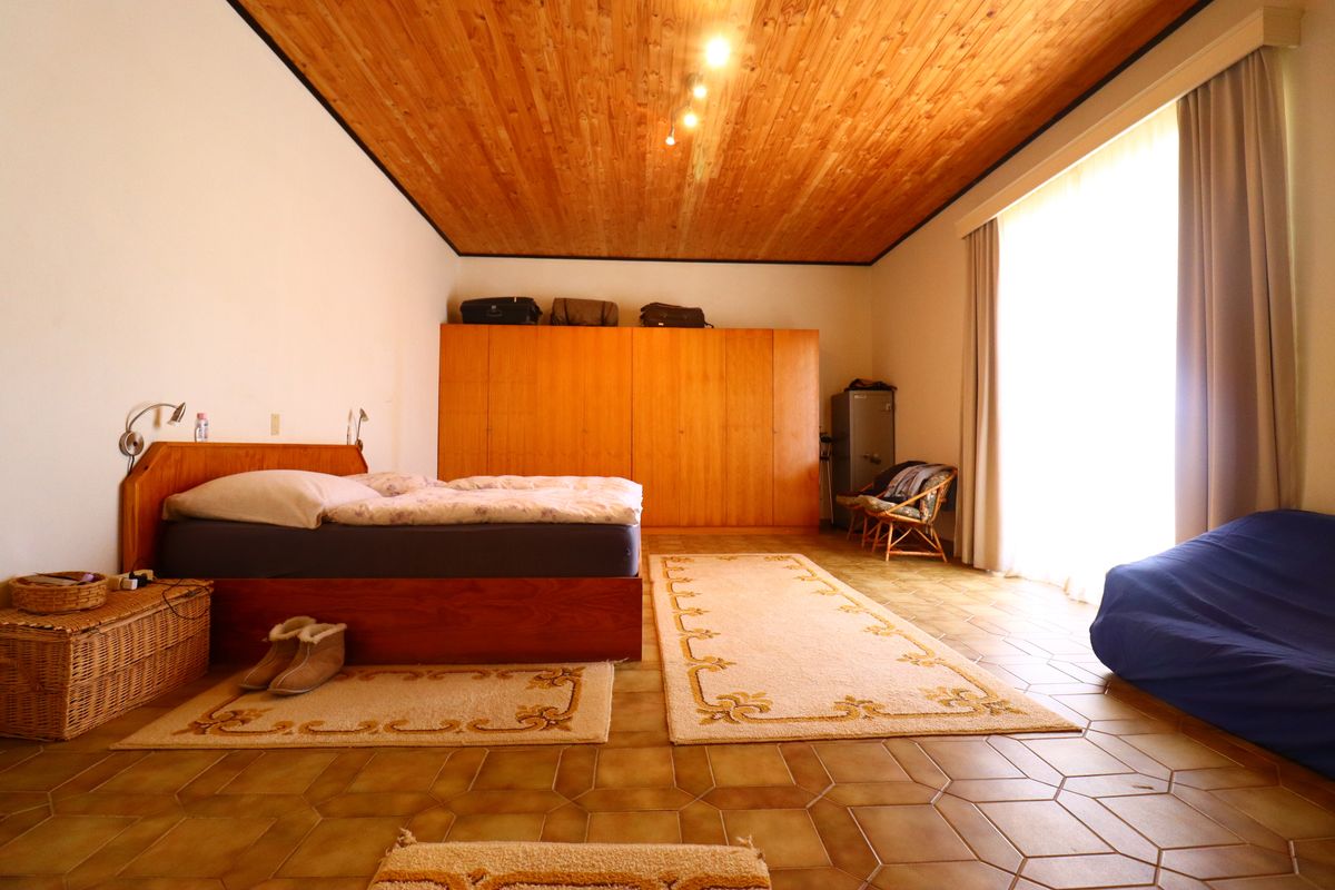 Spacious bedroom featuring a high timber-clad ceiling, tiled flooring, and extensive built-in wooden cabinetry with direct access to the outdoors.