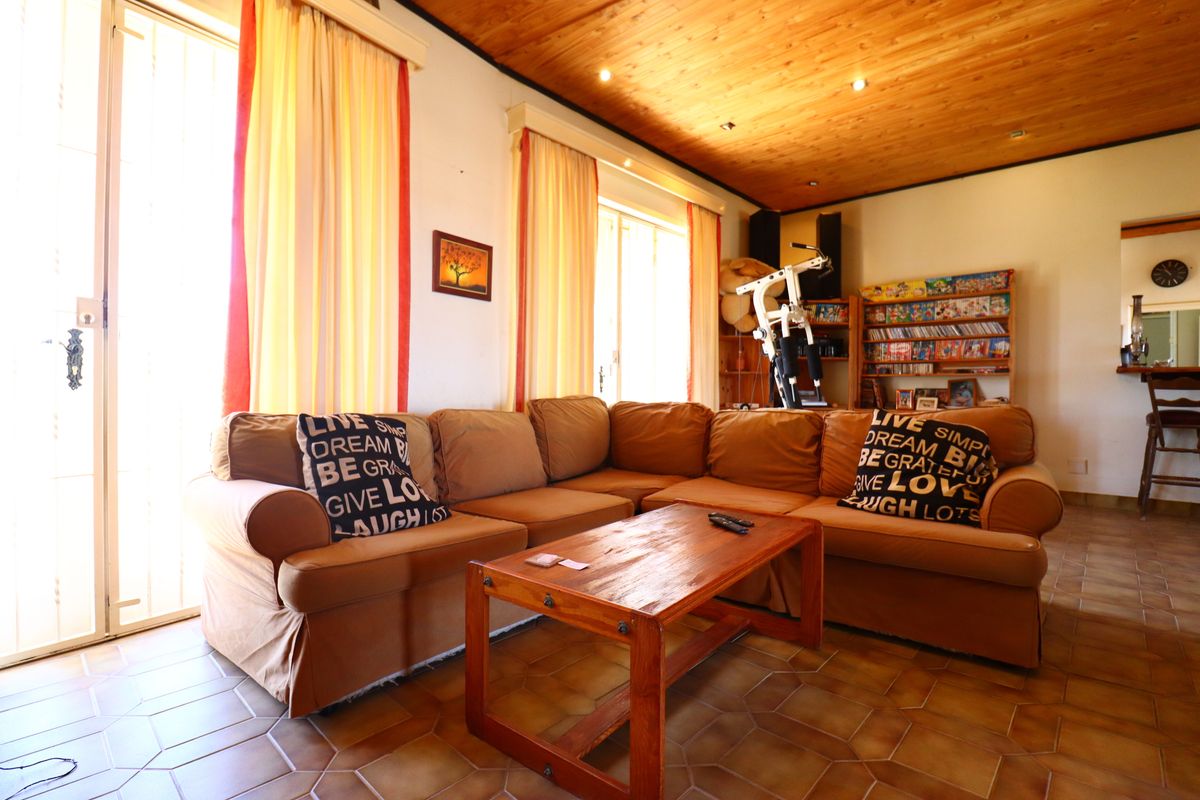 A spacious living room featuring a warm timber-clad ceiling, tiled flooring, and large windows that provide ample natural light.