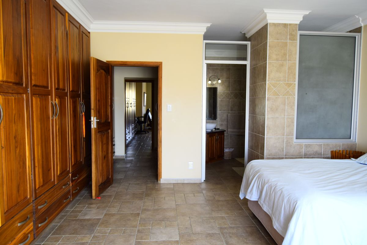 Spacious bedroom featuring built-in wooden cabinetry, tiled flooring, crown molding, and an en-suite bathroom with tiled wall finishes.