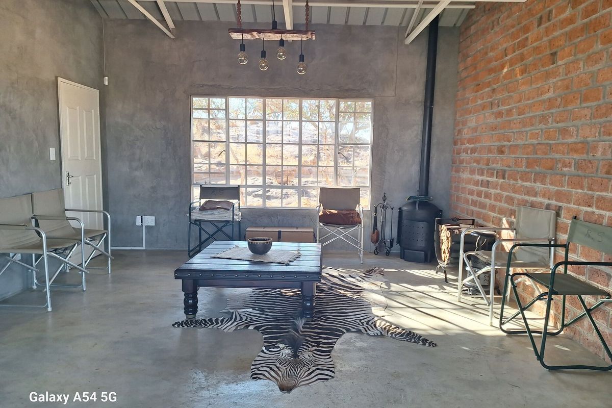Rustic living area featuring exposed brick walls, polished concrete flooring, a wood-burning fireplace, and large windows providing natural light.