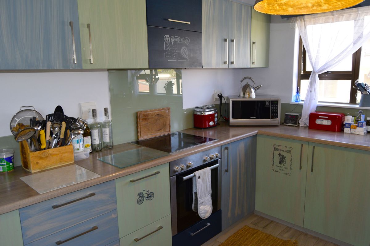 A functional kitchen featuring laminate countertops, a built-in electric oven and hob, glass splashback, and ample storage cabinetry.