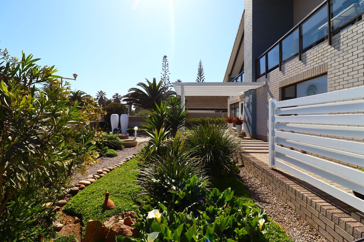 A well-maintained rear garden featuring a paved walkway, modern white pergola, and established landscaping alongside the brick exterior of the house.