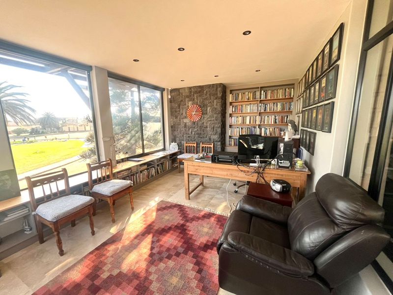 A bright home office featuring large windows with garden views, built-in floor-to-ceiling bookshelves, and a striking stone-clad feature wall.