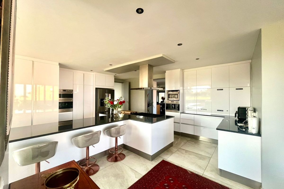 Modern kitchen featuring high-gloss white cabinetry, black stone countertops, a central island with breakfast bar, and integrated stainless steel appliances.