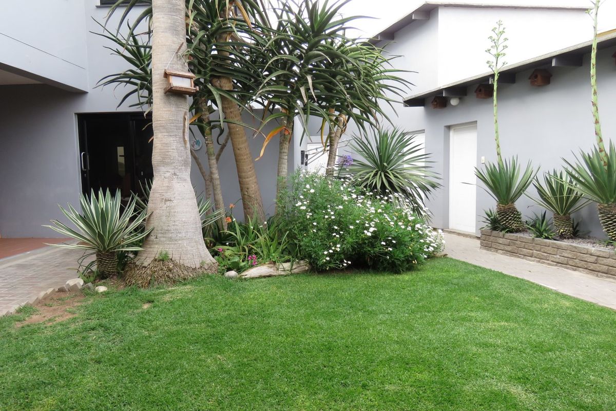 A well-maintained rear garden area featuring a manicured lawn, established landscaping, and paved pathways connecting the exterior building elevations.