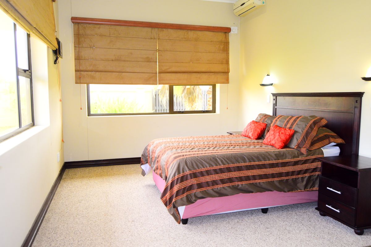 A well-lit bedroom featuring neutral carpeting, large windows with fitted blinds, and a wall-mounted air conditioning unit.