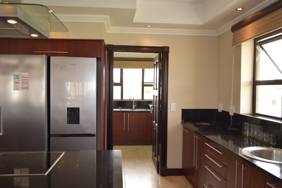 A well-appointed kitchen featuring dark wood cabinetry, black granite countertops, a stainless steel extractor fan, and a separate scullery area visible through the doorway.