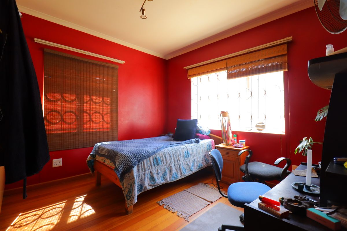 A bedroom featuring timber flooring, security bars on windows, and bold red wall paint, providing a functional space with natural light.
