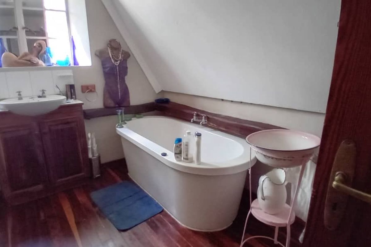 Bathroom featuring a freestanding bathtub, timber vanity cabinet with integrated basin, and hardwood flooring under a sloped ceiling.