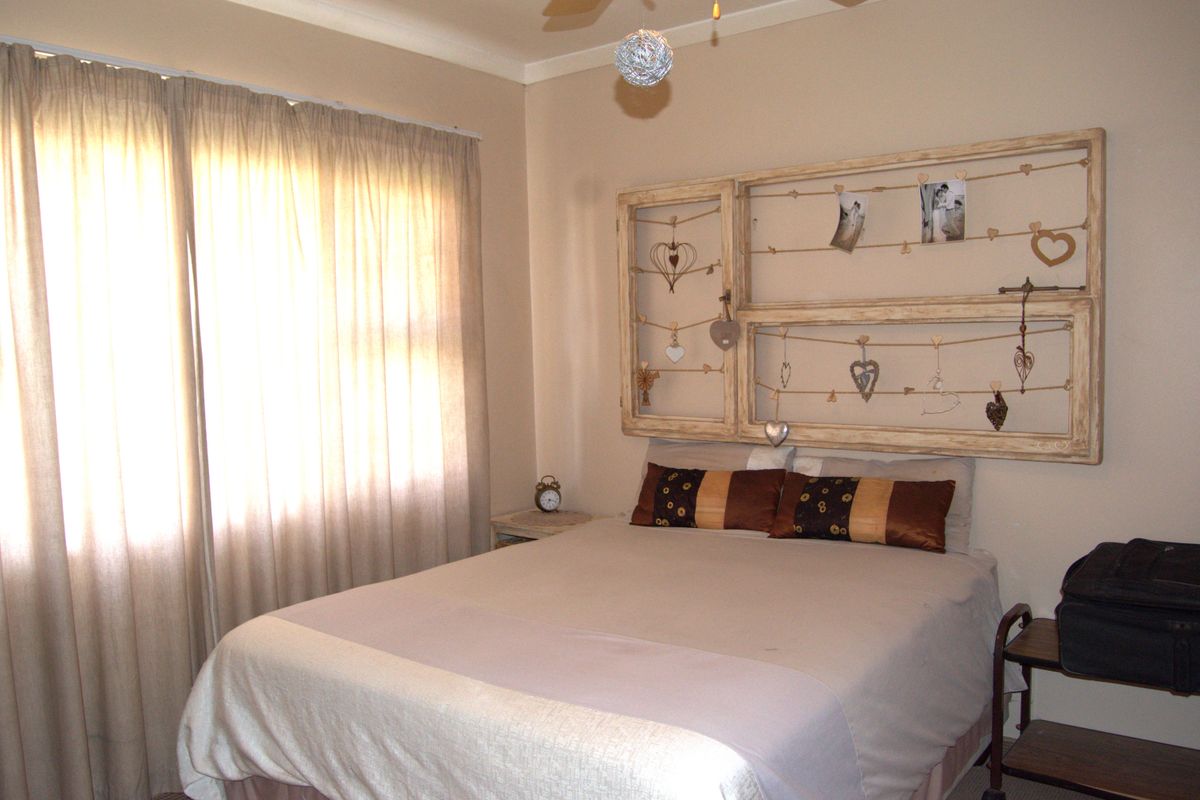 A standard bedroom featuring neutral wall tones, a ceiling fan, and large windows with installed curtain rails.