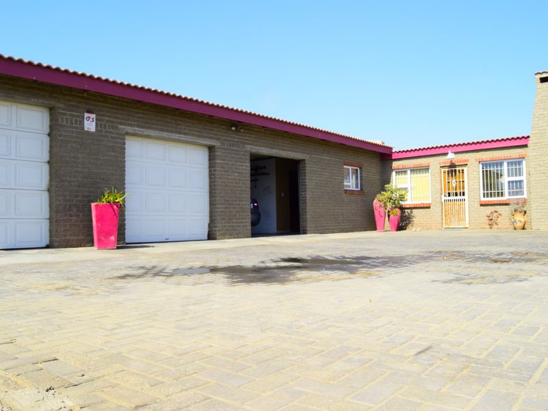 Front exterior view of the property featuring a large paved driveway, double garage access, and brick facade with security entrance.