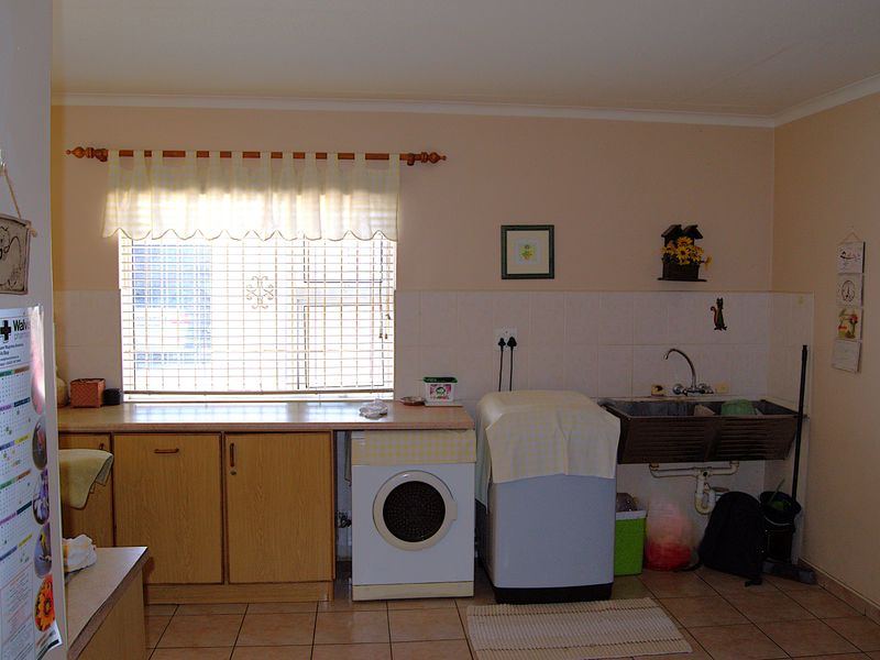 Functional laundry room featuring built-in cabinetry, laminate countertops, a utility sink, and tiled flooring with a window for natural light.