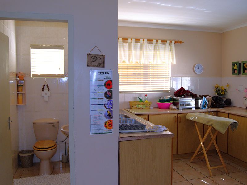 Open plan kitchen area featuring laminate cabinetry and countertops, adjacent to a tiled bathroom with a toilet and pedestal basin.