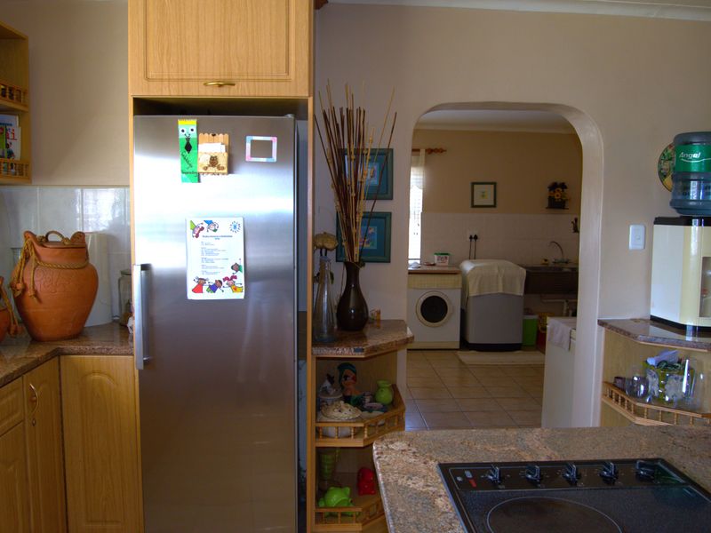 A functional kitchen featuring wood-finish cabinetry, granite countertops, and an electric hob, with an arched opening leading to an adjacent laundry area.