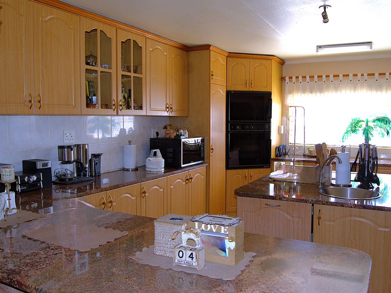 Spacious kitchen featuring granite countertops, a central island with sink, built-in double oven, and ample wooden cabinetry with a tiled backsplash.