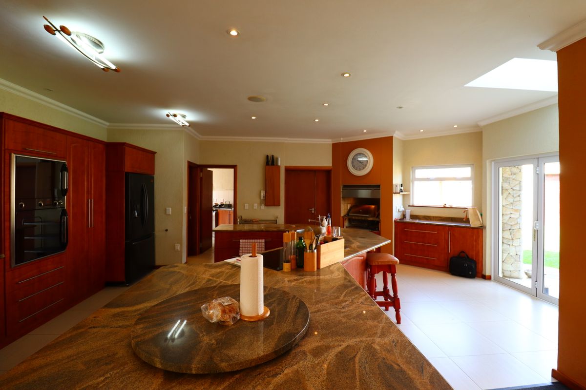 Spacious kitchen featuring cherry wood cabinetry, granite countertops, a central island, built-in oven, and integrated braai area with direct access to the patio.