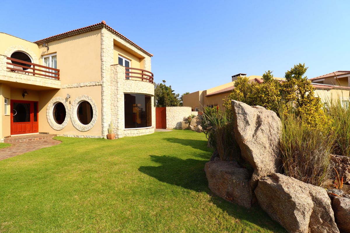 A well-maintained exterior view of a Mediterranean-style house featuring stone cladding, circular windows, and a landscaped garden with large decorative rock features.