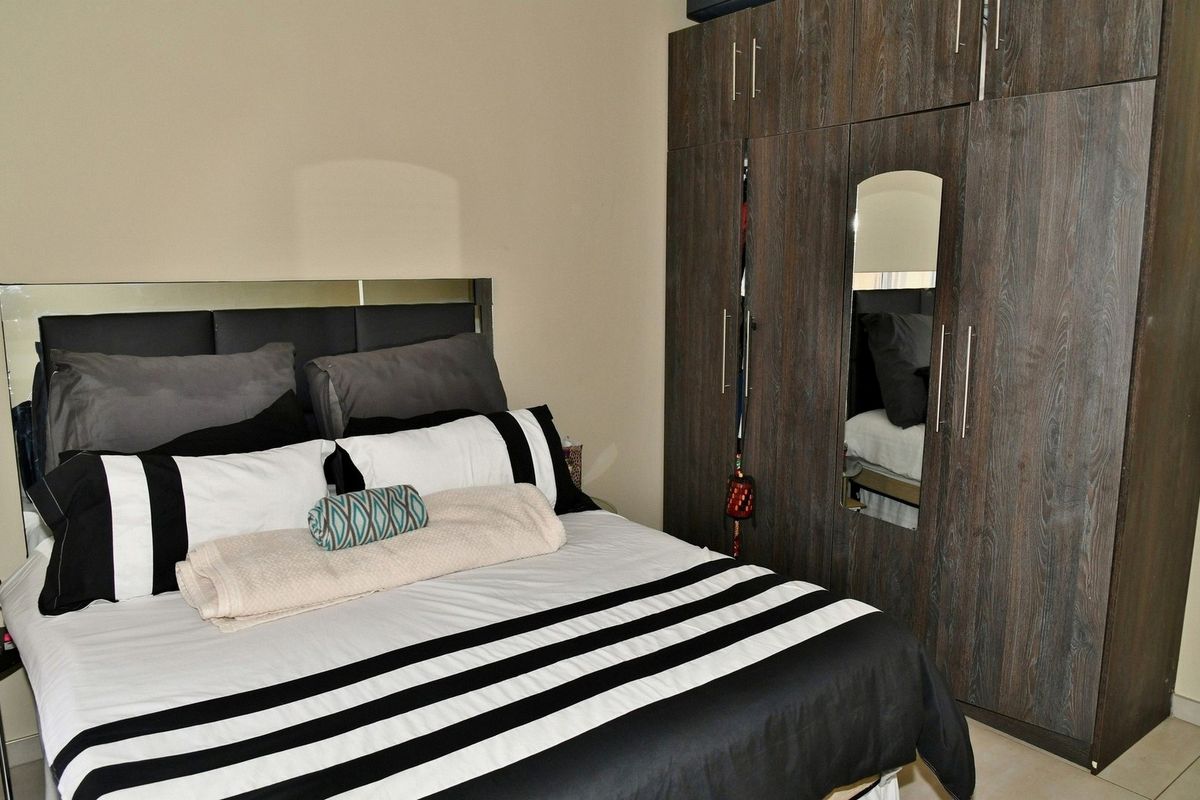 A bedroom featuring built-in dark wood-grain wardrobes with a central mirror and a modern headboard.