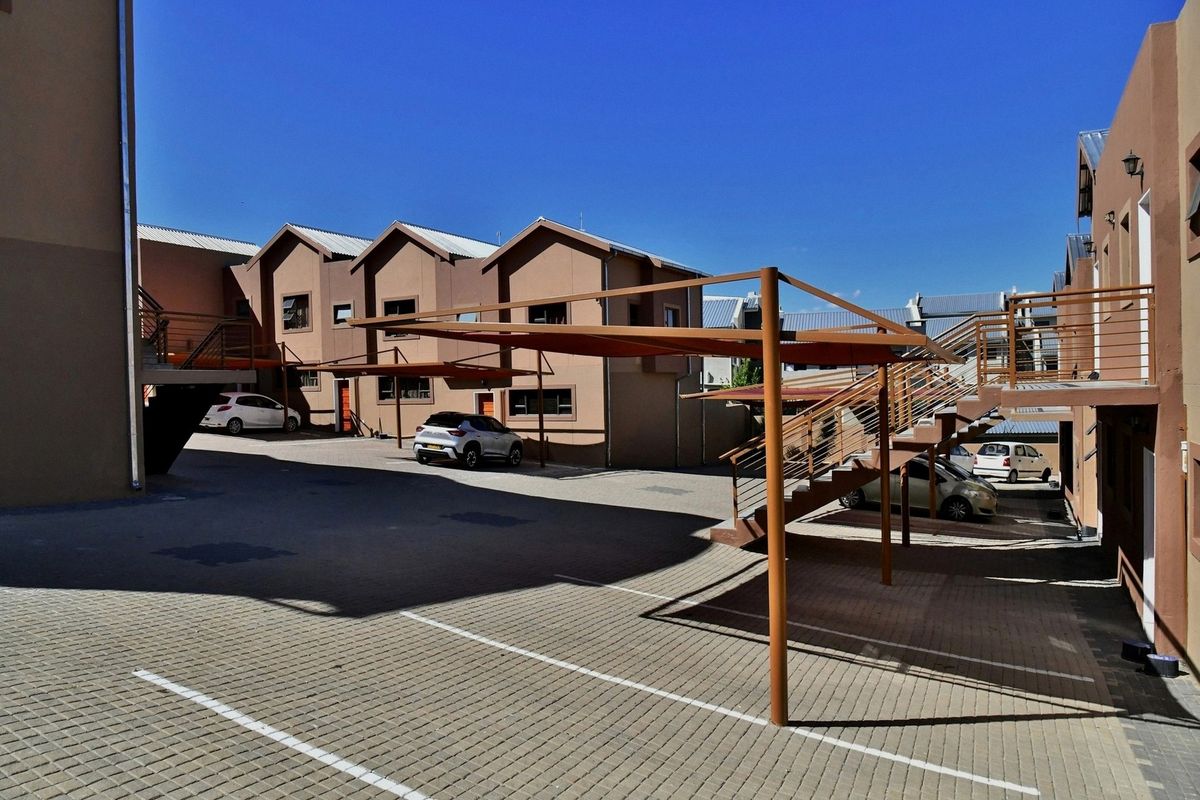 Exterior view of the apartment complex courtyard featuring paved parking areas, covered carports, and external staircases providing access to upper-level units.