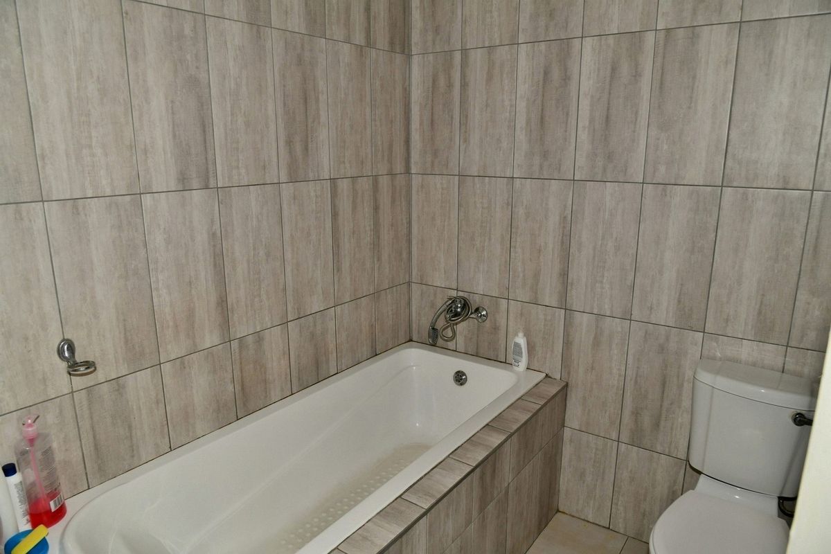 A functional bathroom featuring a built-in bathtub with wall-mounted mixer tap and a standard toilet, finished with neutral wood-look wall tiling.
