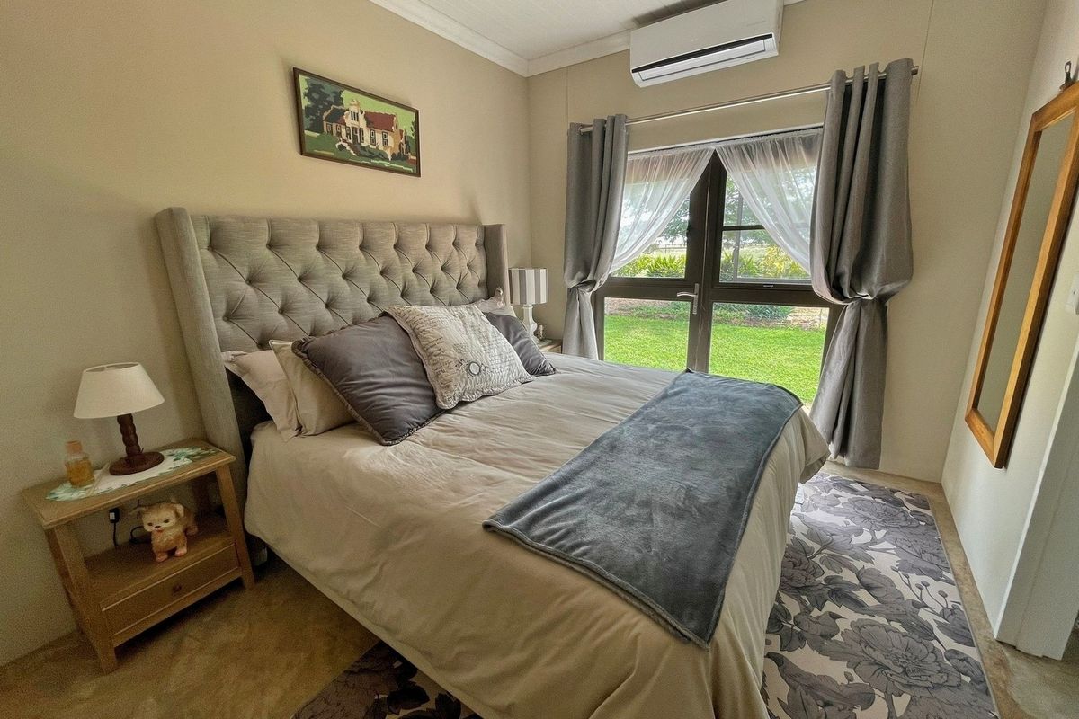 A well-maintained bedroom featuring a wall-mounted air conditioning unit, large window with garden views, and neutral finishes.