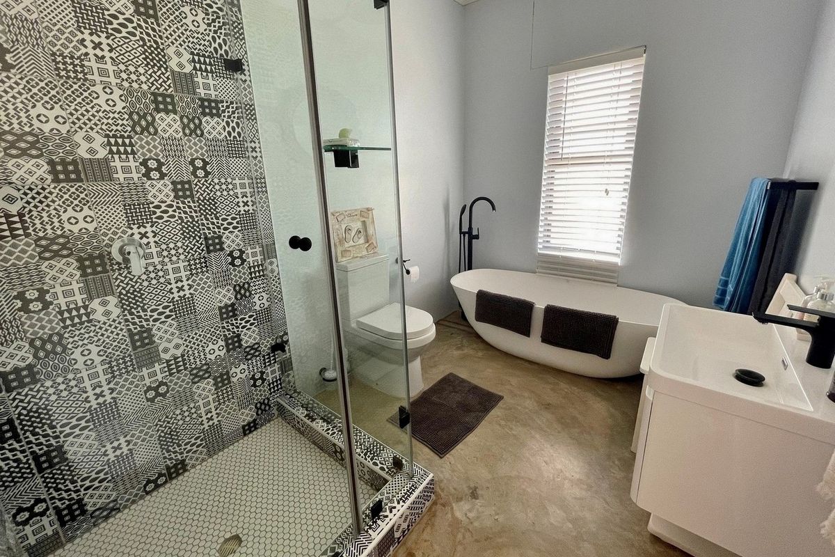 Modern bathroom featuring a walk-in shower with patterned tile accents, a freestanding bathtub, a contemporary vanity, and polished concrete flooring.
