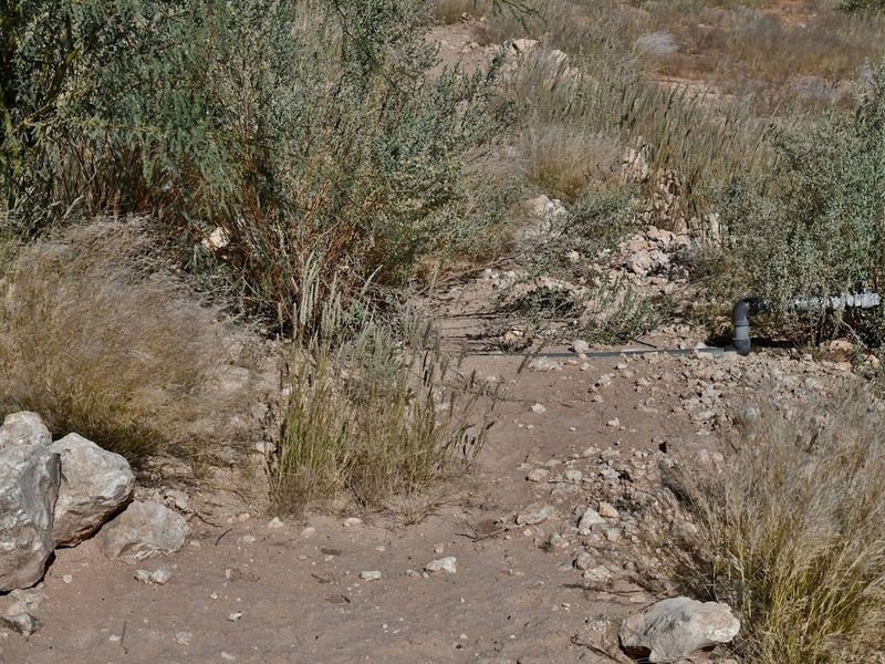 An undeveloped area of the small holding featuring exposed irrigation piping and natural, unlandscaped terrain.