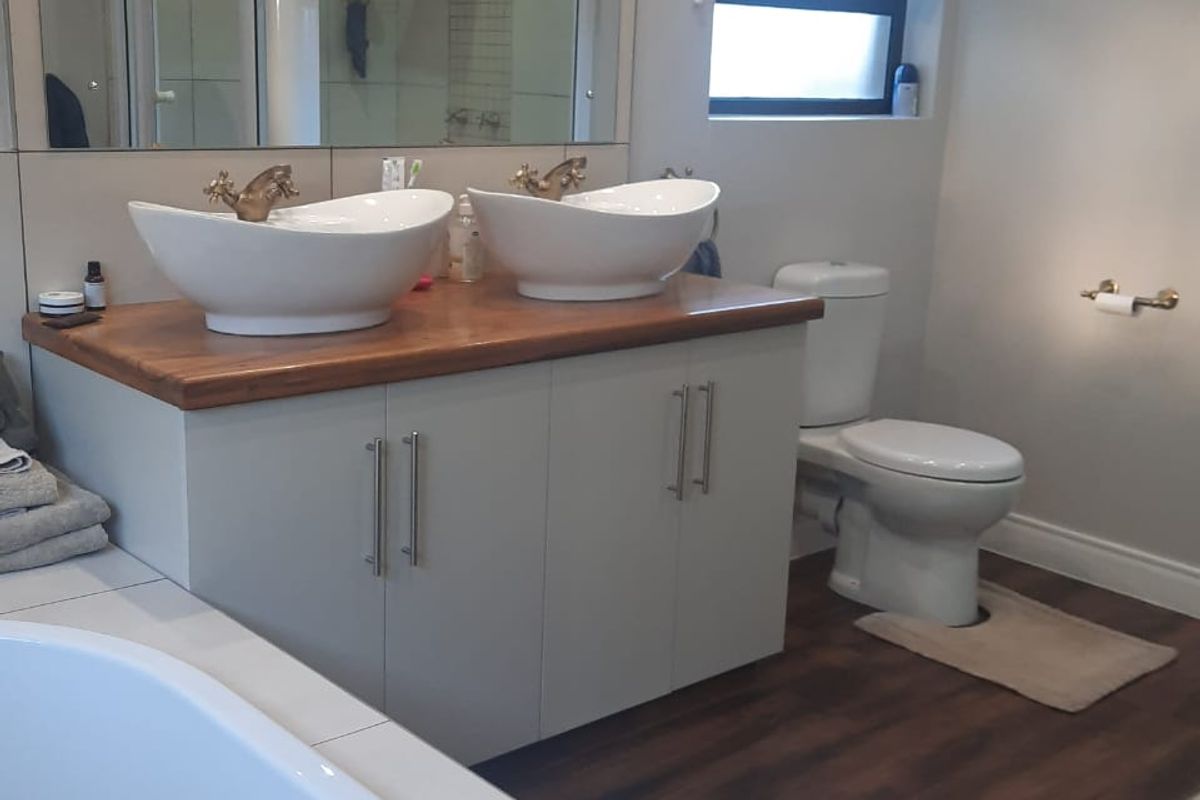 Modern bathroom featuring a double vanity with vessel sinks, wooden countertop, large wall mirror, toilet, and a separate bathtub.