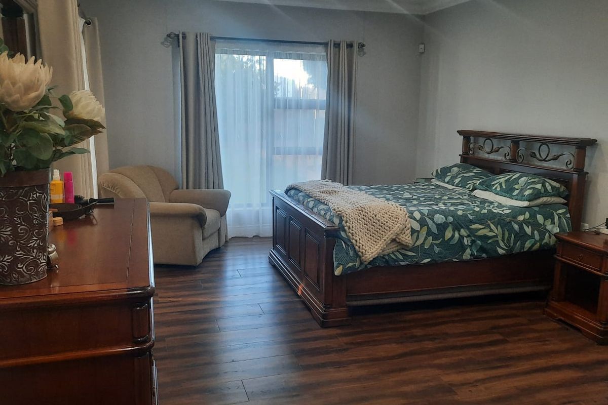 A spacious bedroom featuring dark wood-look laminate flooring, neutral walls, and large windows with curtains, providing a comfortable and well-maintained living space.